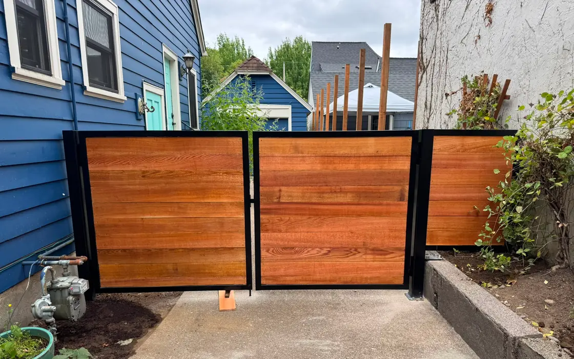 Horizontal cedar swing gate in steel frame viewed from driveway between blue and stucco houses. Fence & gate installation in Battle Ground
