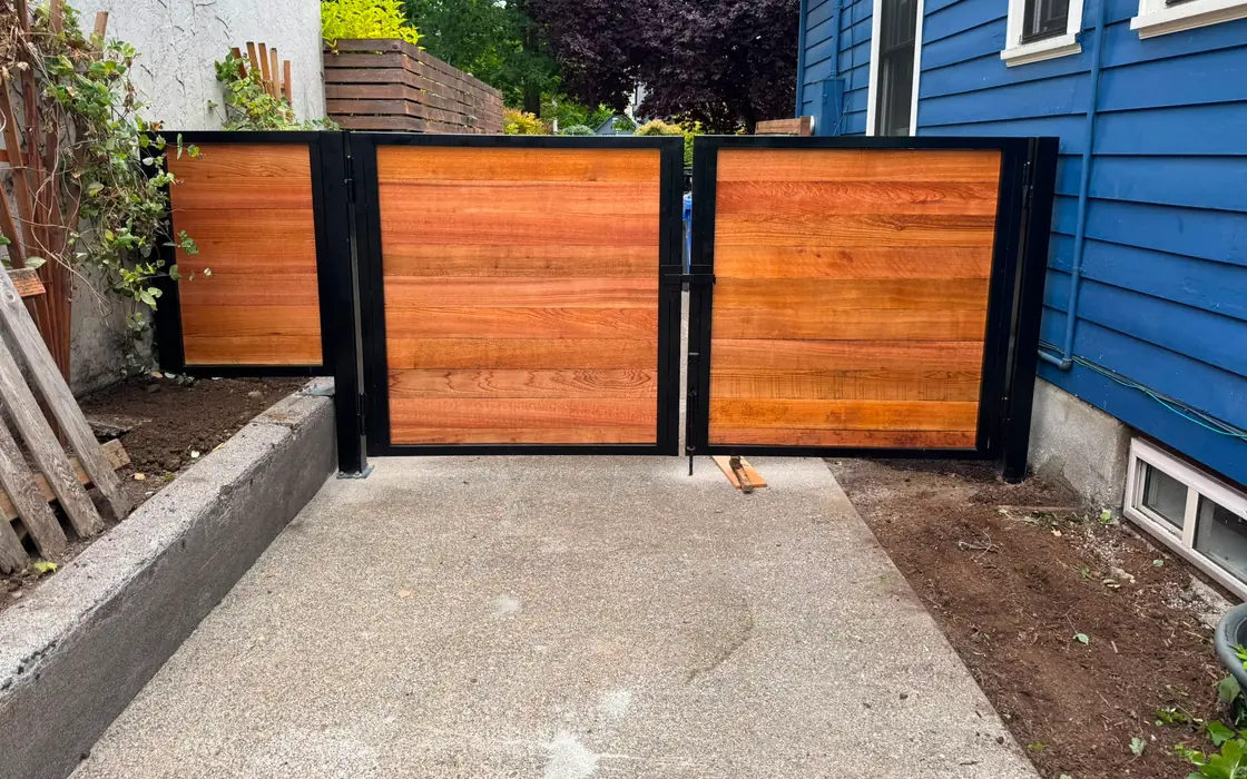 Horizontal cedar double swing driveway gate in black steel frame between houses. Fence & gate installation in Camas