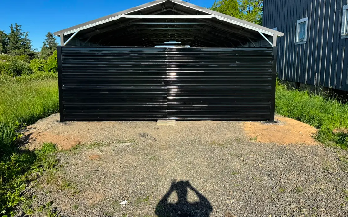 Black metal double swing gate on steel carport, exterior, clear sky. Fence & gate installation in Canby