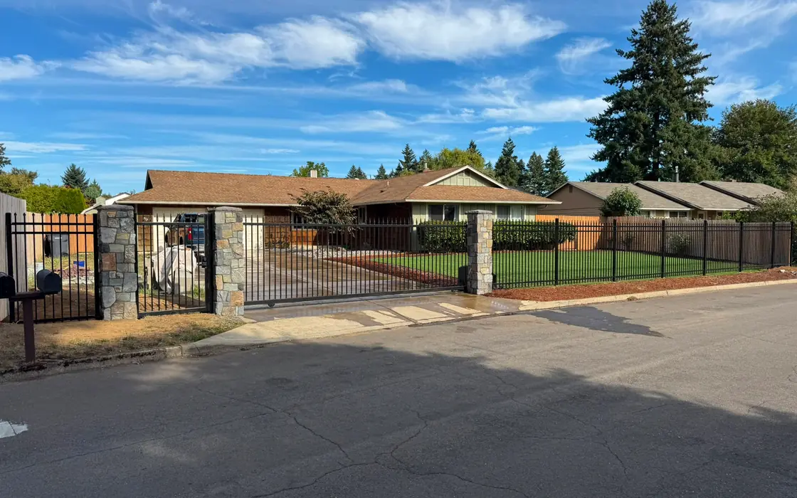Wide view of ranch home behind black iron fence, stone columns and slide gate. Fence & gate installation in Happy Valley