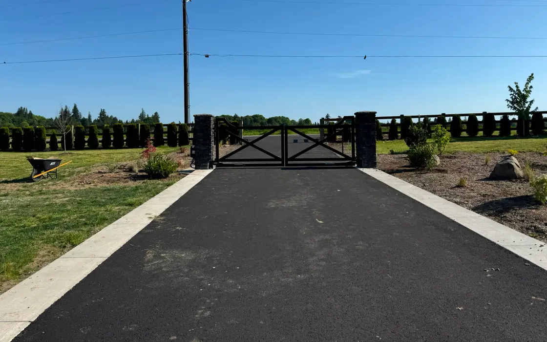 Black X-brace driveway gate with stone columns viewed across farm field. Fence & gate installation in Hazel Dell