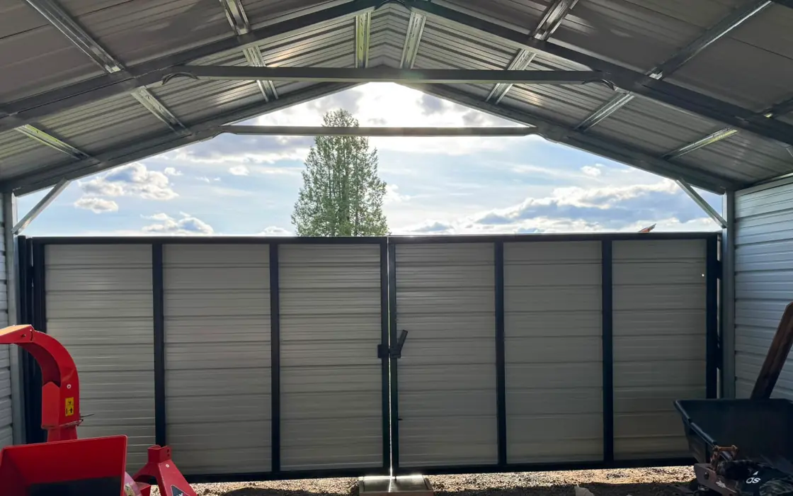 Beige metal swing gates with center latch inside steel carport bay. Fence & gate installation in Kalama