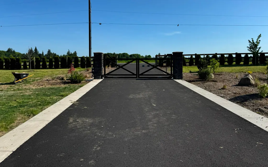 Distant view of black driveway gate with stone columns along ranch fence. Fence & gate installation in La Center