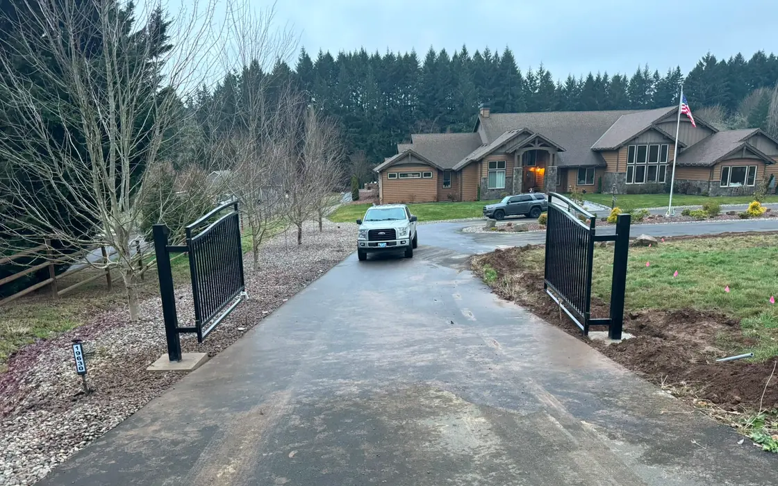 Finished black metal double swing driveway gate open, truck and large home behind. Fence & gate installation in Milwaukie