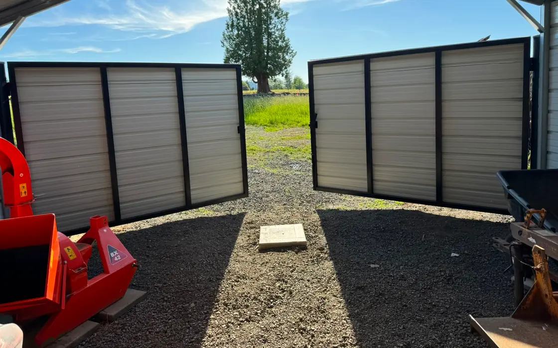 Tan metal swing gates open at end of steel farm carport, field view. Fence & gate installation in Newberg