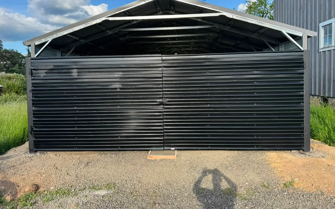 Black metal double swing gate on open-topped steel carport, sunny. Fence & gate installation in Ridgefield