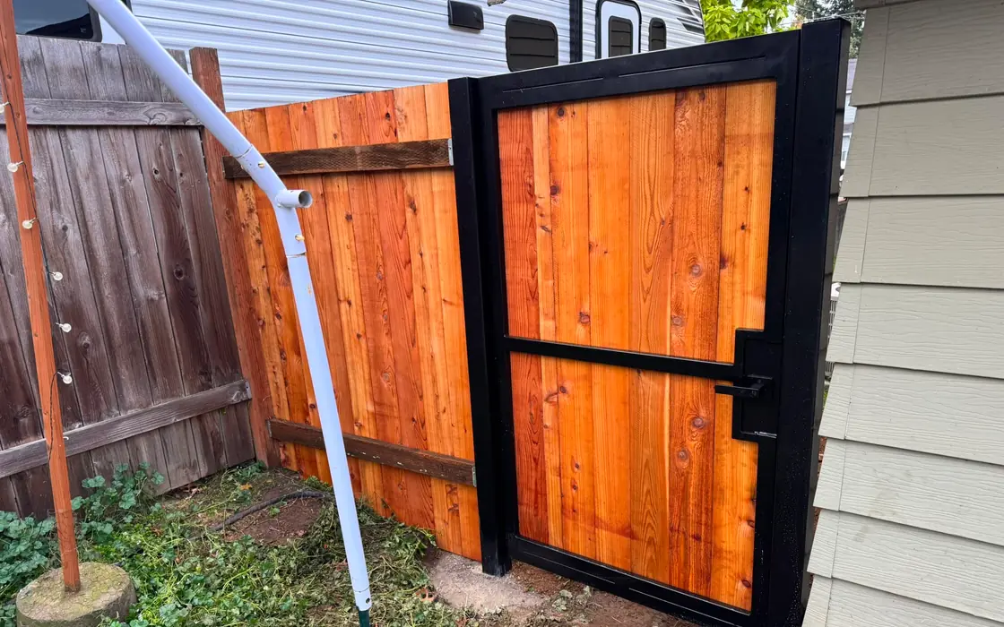 Black steel-frame cedar pedestrian gate between house and older wood fence, install area. Fence & gate installation in St. Helens