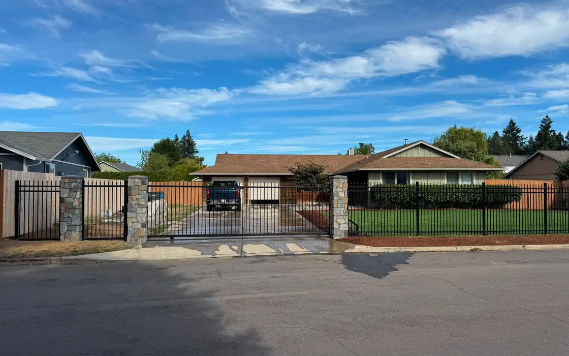 Front street view of ranch home with black iron fence, slide gate and stone pillars. Fence & gate installation in Vancouver