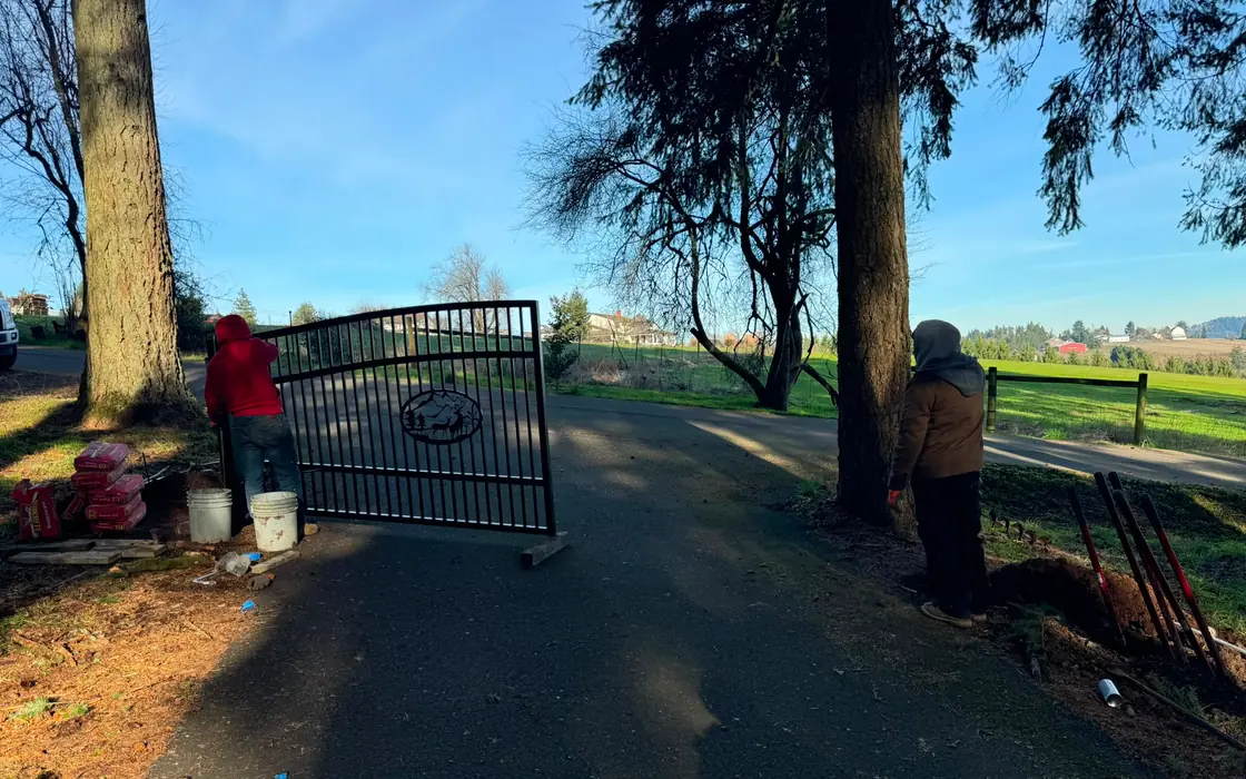 Black metal driveway gate with mountain elk emblem staged at rural entrance. Fence & gate installation in Woodland