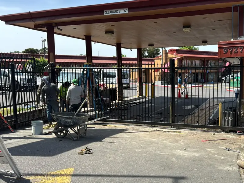 Access-controlled gate. Black ornamental iron security gate and fencing at motel drive-through, mid installation