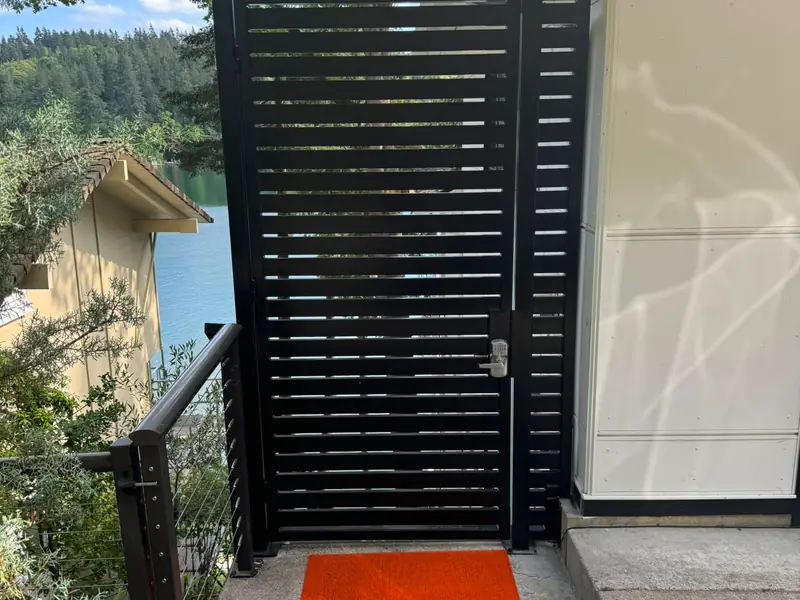 Modern horizontal-slat fence. Black horizontal-slat metal pedestrian gate with keypad lock at lakeside home entry