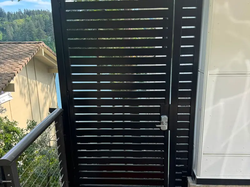Black aluminum slat fence. Black horizontal-slat pedestrian gate with keypad deadbolt on concrete landing
