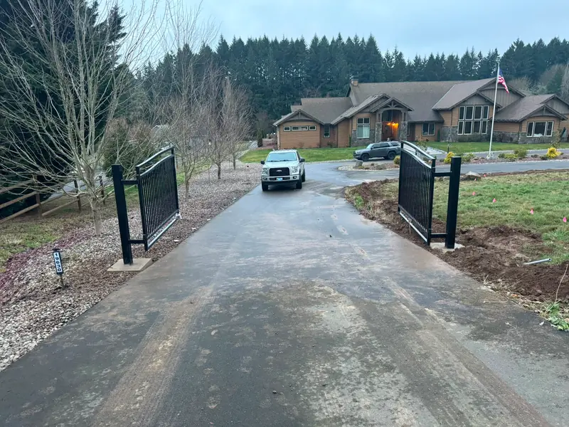 Driveway entry gate. Finished black metal double swing driveway gate open, truck and large home behind