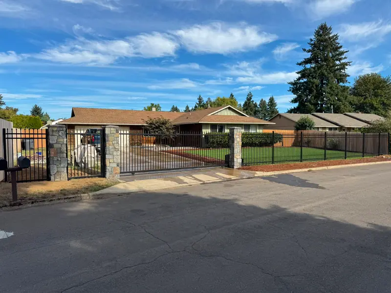 Full property enclosure. Wide view of ranch home behind black iron fence, stone columns and slide gate