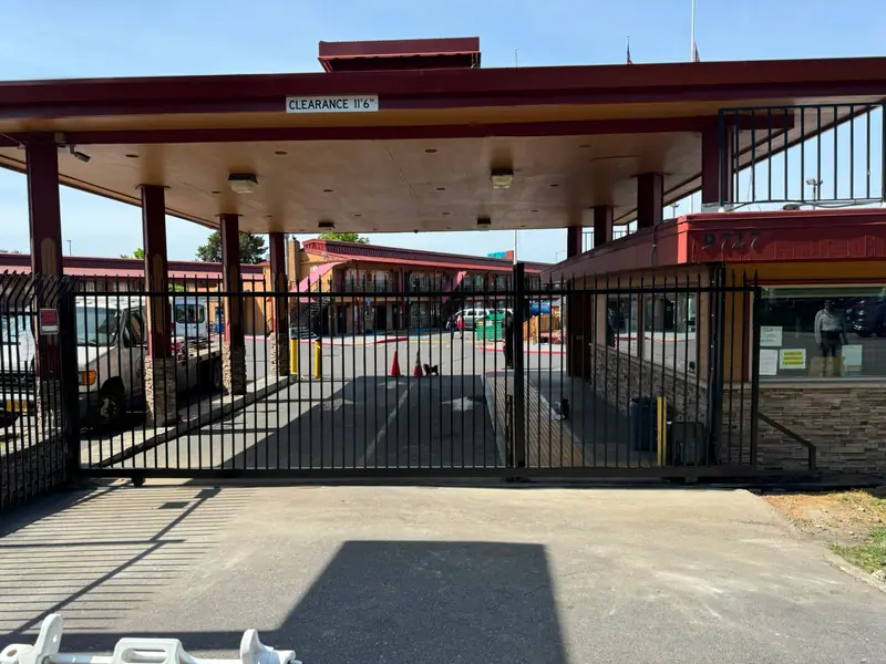 Wide view of motel entrance with black ornamental iron slide gate and canopy. Chain Link Fencing in Portland