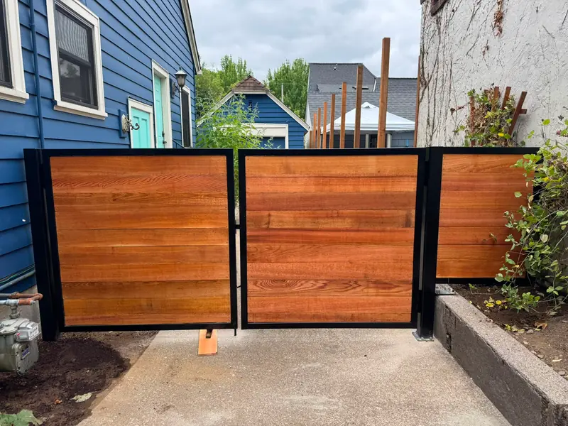 Horizontal cedar wood swing gates with black steel frames between houses. Custom Driveway & Yard Gates in Portland