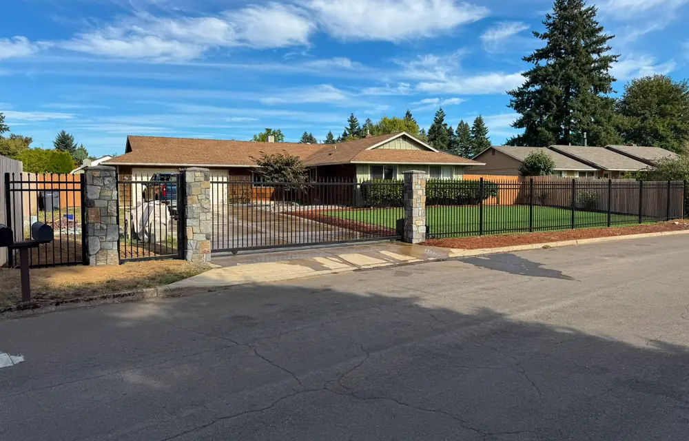 Wide view of ranch home behind black iron fence, stone columns and slide gate. Fencing in Cascade Park