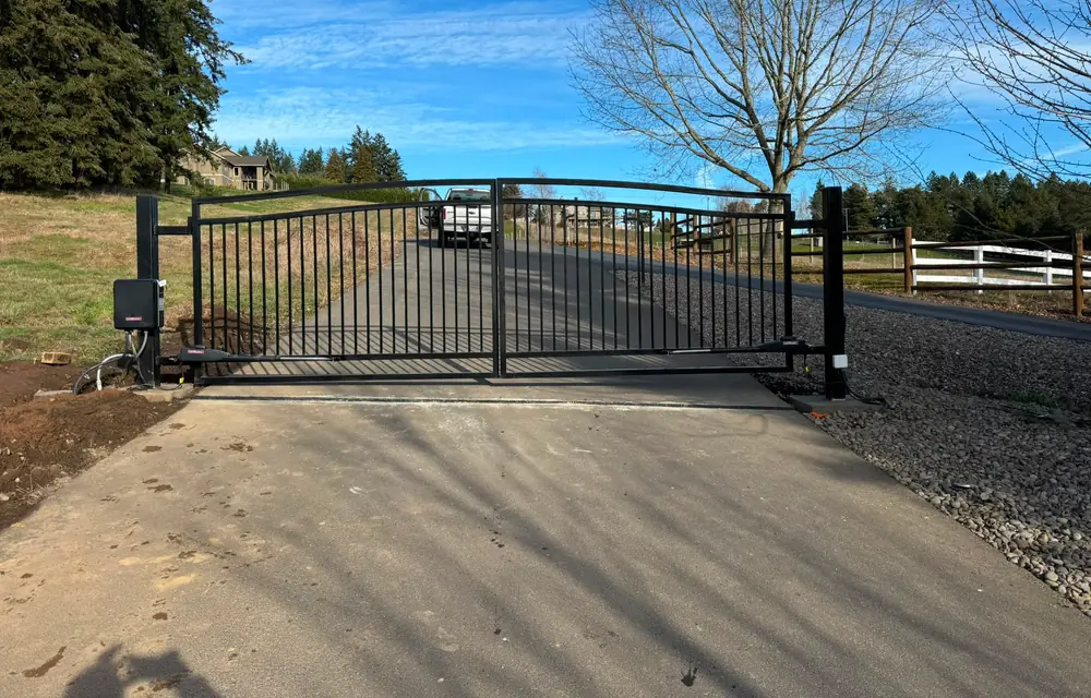 Closed black steel dual-swing driveway gate with LiftMaster operators on concrete apron. Fencing in Charbonneau