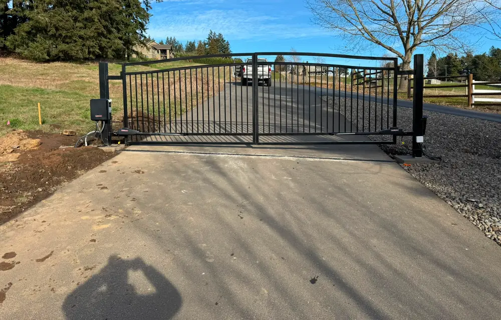 Closed dual-swing black metal driveway gate with LiftMaster operators, blue sky. Fencing in Hockinson