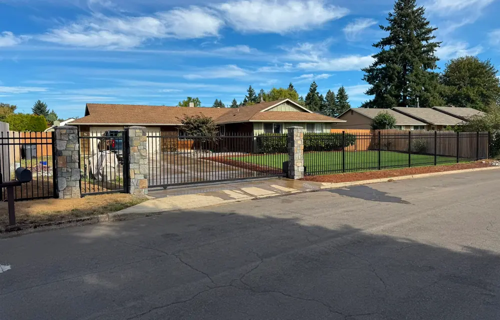 Wide street view of ranch home enclosed by black iron fence with stone columns. Fencing in Old Town Sherwood