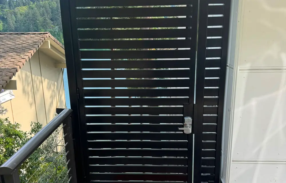 Black horizontal-slat pedestrian gate with keypad deadbolt on concrete landing. Fencing in Prune Hill