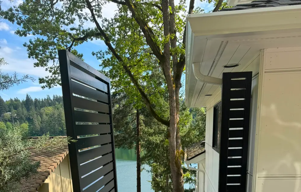 Open black horizontal-slat gate revealing lake view at hillside entry. Fencing in Rockwood