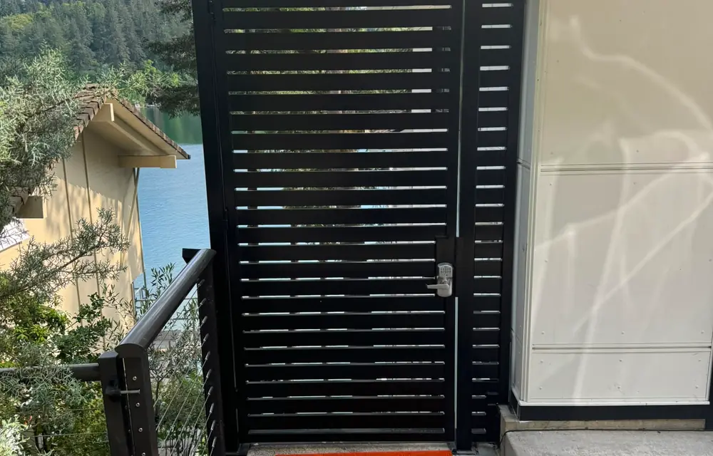 Black horizontal-slat metal pedestrian gate with keypad lock at lakeside home entry. Fencing in Sellwood-Moreland