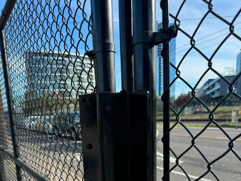 Closeup of black vertical gate operator hardware on chainlink gate post, city street