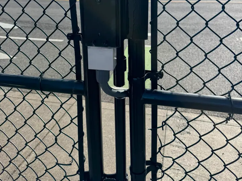 Closeup of vertical ram operator on black chainlink swing gate, city buildings behind