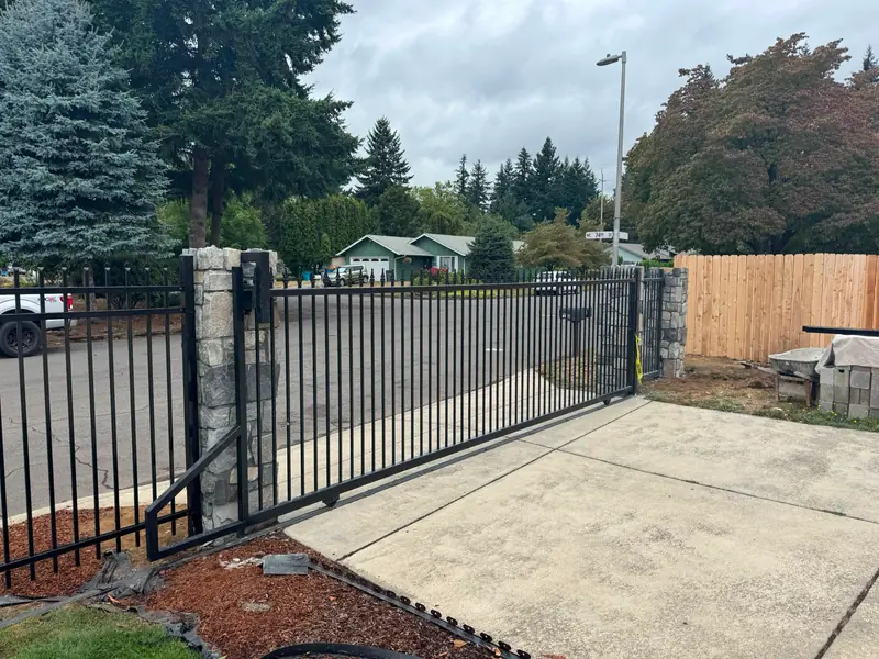 Black ornamental iron slide gate with stone columns across residential driveway