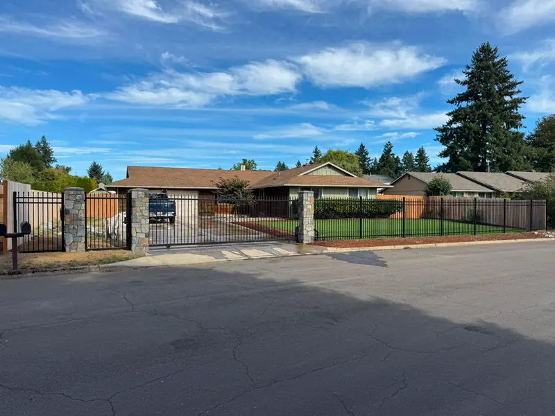 Wide view of ranch home with black iron fence, slide gate and stone columns on lawn