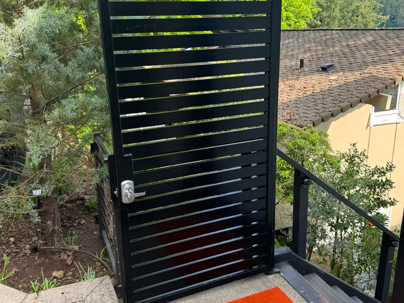 Black horizontal-slat metal gate on hillside stairs above rooftops